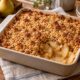 Pear and apple ginger crumble with a golden oat topping in a ceramic baking dish, with a portion scooped out to reveal the tender fruit.